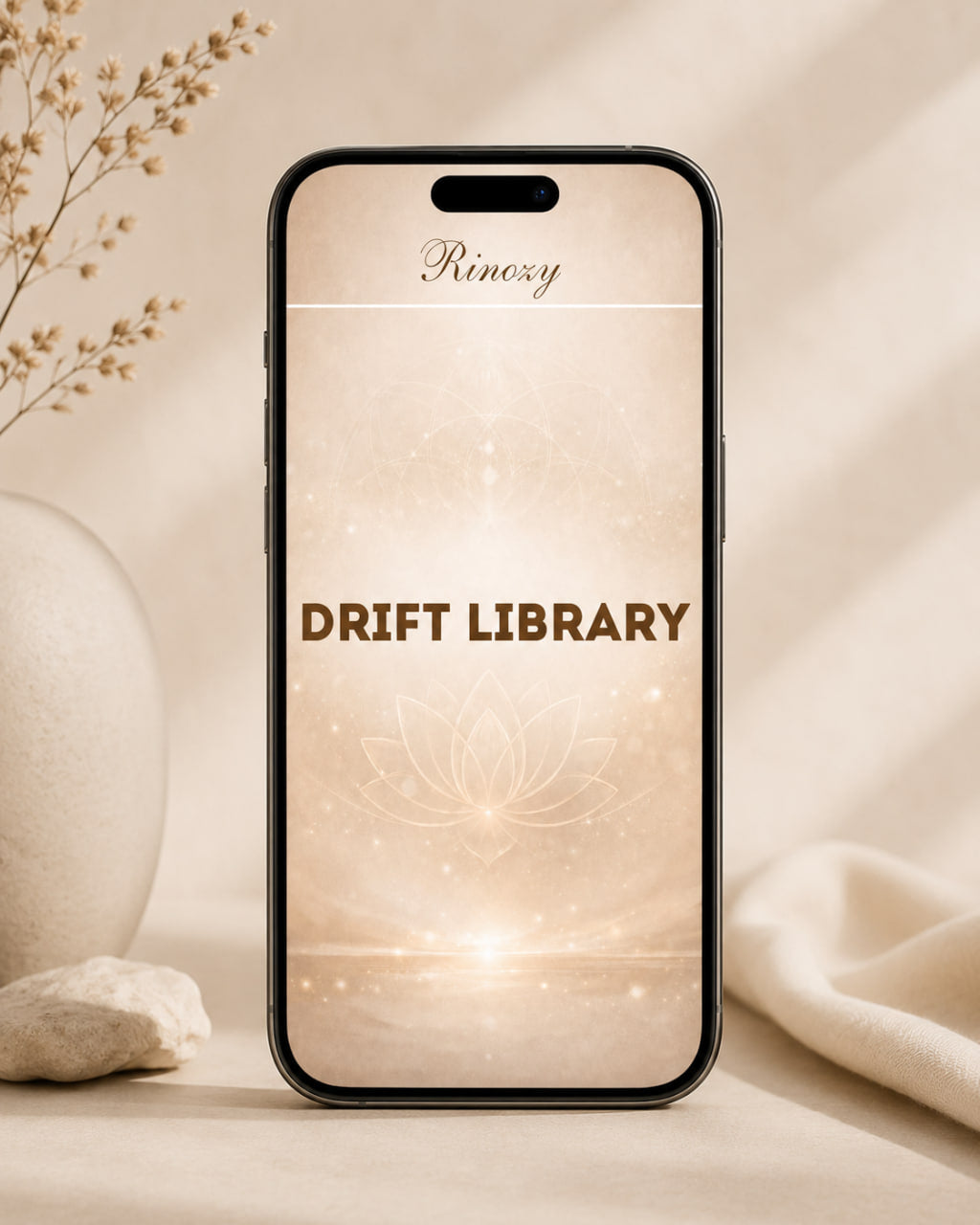 A smartphone centered on a warm beige surface with soft decorative props, displaying a minimalist app-style screen that reads 'Rinoy' at the top and 'DRIFT LIBRARY' in brown text with a glowing lotus motif below.